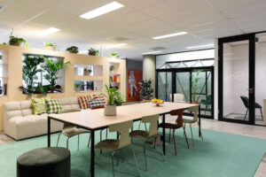 Moderne kantoorruimte aan de Johan Huizingalaan met een gemeenschappelijke zithoek, grote tafel, veel planten en glazen vergaderruimte.